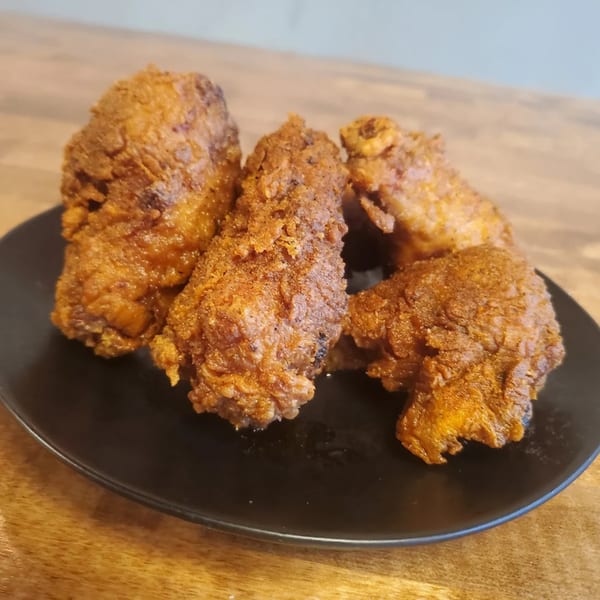 Four pieces of crispy, golden-brown Fire Nashville Hot Chicken on a black plate.