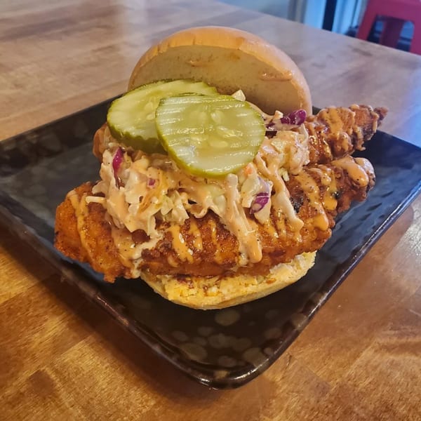 Fire Nashville Hot Chicken sandwich with pickles, coleslaw, and special sauce on a dark plate.